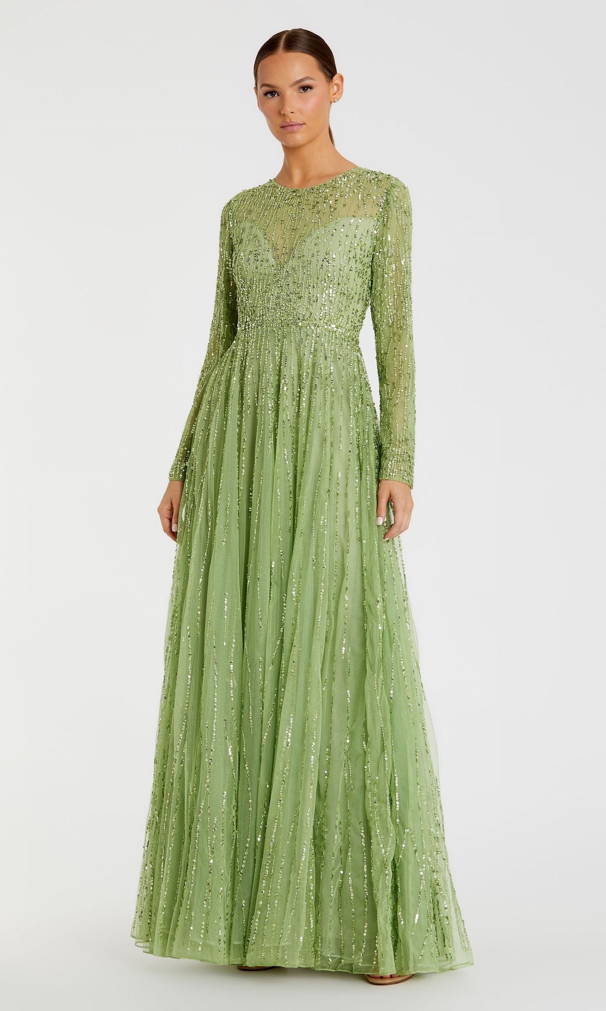 A woman models the Modest Long Sleeve Formal Dress: Mac Duggal 5636 in light green, featuring intricate beading and a floor-length flowing skirt, set against a plain background.